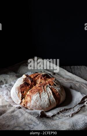 Laib frisches Land Sauerteig Brot auf Stück gelegt Holz auf schäbigen Tisch vor schwarzem Hintergrund Stockfoto