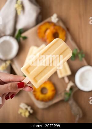 Hand der anonymen Frau hält Kokosnuss-und Ananas-Eis Zu unscharfer Tisch Stockfoto