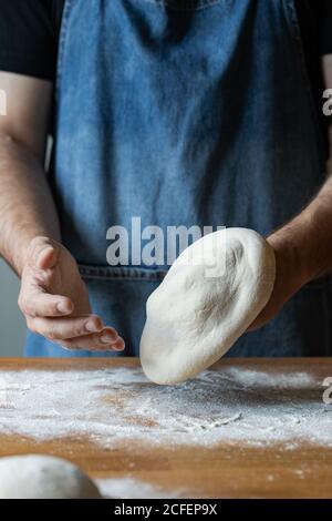 Unkenntlich Männchen in Schürze Abflachung weichen Teig über Tisch mit Mehl beim Kochen Pizza Stockfoto