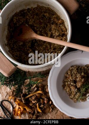 Pfanne und Teller mit köstlichem Reisrisotto mit Kaninchenfleisch Und Pilze mit frischem Rosmarinzweig in der Küche dekoriert Stockfoto