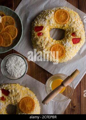 Schüsseln mit frischem Eigelb und Zuckerkristallen Holztisch in der Nähe von köstlichen Rosca de Reyes mit kandierten Früchten Und Samen Stockfoto