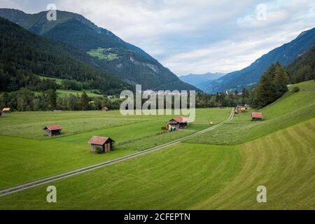 Schöne Bauernhof Hütten in der Nähe von Straße im grünen Tal gegen Bergrücken am bewölkten Tag in Österreich Stockfoto