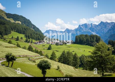 Schöne Bauernhof Hütten in der Nähe von Straße im grünen Tal gegen Bergrücken am bewölkten Tag in Österreich Stockfoto