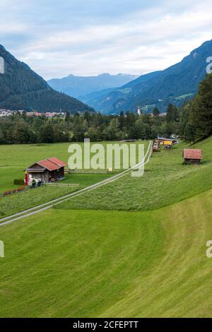 Schöne Bauernhof Hütten in der Nähe von Straße im grünen Tal gegen Bergrücken am bewölkten Tag in Österreich Stockfoto