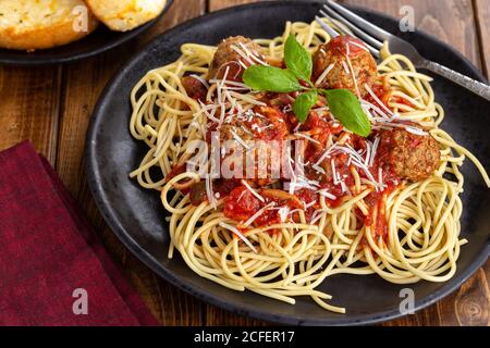 Spaghetti und Fleischbällchen mit Tomatensauce und Parmesankäse Ein schwarzer Essteller Stockfoto