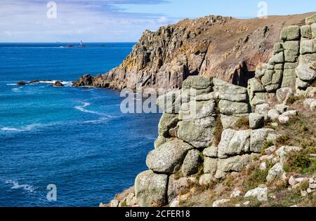 Detaillierte Ansicht der Granite Cliff of Pendower Coves mit höherer Bosistow Cliff, Coast Path und entferntem Longships Lighthouse; Cornish Coast in der Nähe von Lands End. Stockfoto