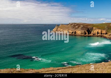 Blick auf die Brandung, die in Nanjizel oder Mill Bay mit Carn Boel, Cliff, Coast Path, und entfernten Longships Leuchtturm; Cornish Coast in der Nähe Lands End. Stockfoto