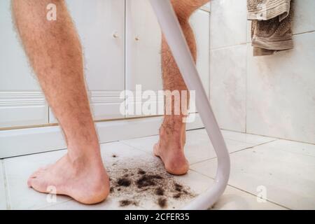 Niedriger Winkel barfuß unkenntlich männlich sitzt auf Stuhl unter Haufen getrimmter dunkler Haare im hellen modernen Badezimmer Zu Hause Stockfoto