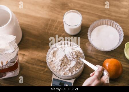 Draufsicht der Ernte anonyme Weizenmehl wägende Frau auf Elektronische Waage während der Zubereitung von Zutaten für köstliche aromatische hausgemachte Muffins In der Küche Stockfoto