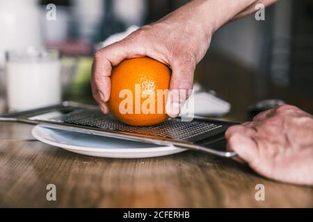 Seitenansicht der Ernte anonyme Frau entfernen Orangenschale mit Reibe während der Zubereitung aromatischer Gebäck in der Küche zu Hause Stockfoto