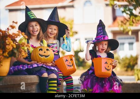 Frohe Halloween! Drei süße kleine lachende Mädchen in Hexen-Kostümen kommen zum Haus für Süßigkeiten. Stockfoto