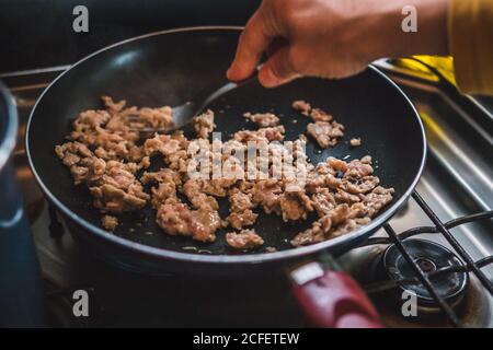 Hand einer anonymen Person, die Hackfleisch mit Gabel aufdrückt Bratpfanne beim Kochen in der Küche Stockfoto