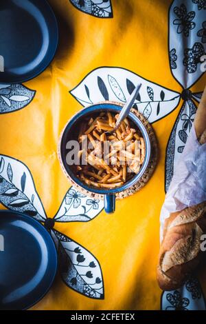 Von oben Tasse mit leckeren Pasta auf dekorative Tischdecke gelegt In der Nähe von Brot und leeren Schüsseln Stockfoto