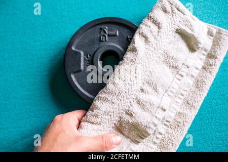 From above crop sportsman placing white towel on black metal weight on turquoise sports mat while preparing for training in light modern gym Stockfoto
