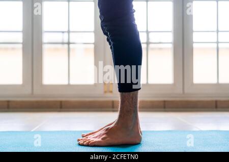 Flache Seitenansicht der Ernte barfuß männlichen Athleten in Aktiver Verschleiß, der in der Startposition steht, während er alleine trainiert Sportmatte gegen Fenster im hellen, geräumigen Raum zu Hause Stockfoto