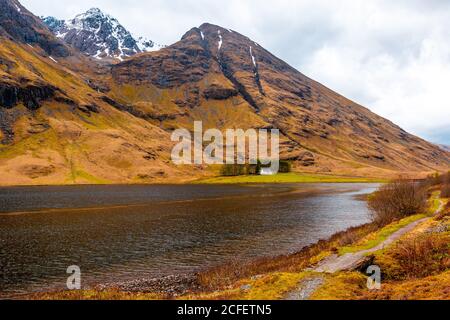 Erstaunliche schottische Landschaft von ruhigen See mit spiegelnden Oberfläche Berg mit schneebedeckten Gipfel und blau bewölkten Himmel in Glen Coe Stockfoto