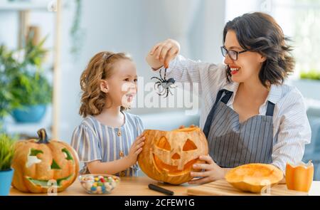 Glückliche Familie bereitet sich auf Halloween vor. Mutter und Kind schnitzen Kürbisse zu Hause. Stockfoto