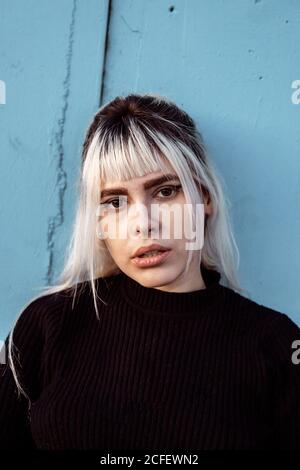 Junge blonde Frau mit langen blonden Haaren trägt schwarzen Pullover Blick auf die Kamera mit unglücklichen und enttäuschten Augen müde Gesicht Stockfoto