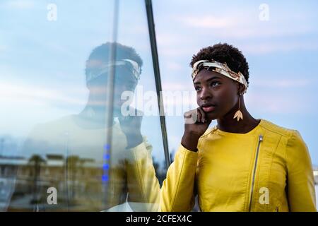 Seitenansicht einer ruhigen afroamerikanischen Frau, die auf dem Glasbalkon chillt und wegschaut Stockfoto