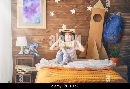 Mädchen in einem Astronaut Kostüm mit Spielzeug Rakete spielen und träumen von einem Raumfahrer zu werden. Portrait von lustigen Kind im Schlafzimmer. Stockfoto