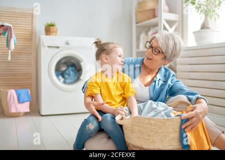 Glückliche Oma und Kind Mädchen kleinen Helfer haben Spaß und lächeln, während die Wäsche zu Hause. Stockfoto