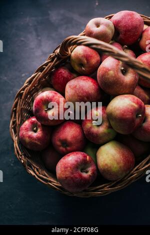 Frische rote Äpfel auf dunklem Tisch und in Weide Korb auf dunklem Hintergrund Stockfoto