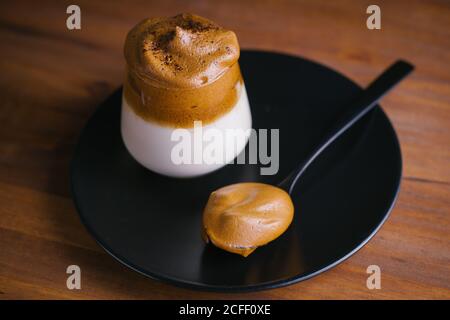 Von oben von leckeren Dalgona Getränk aus kalter Milch zubereitet Und peitschten Kaffee auf einem Glas auf einem schwarzen platziert Platte auf einem Holztisch Stockfoto