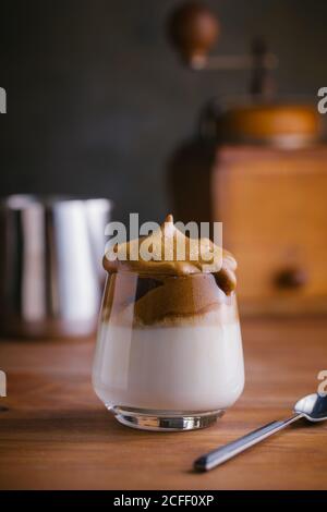 Schlagkaffee Dalgona Kaffee in kalter Milch in der Nähe von Jahrgang platziert Kaffeemühle auf Holztischoberfläche Stockfoto