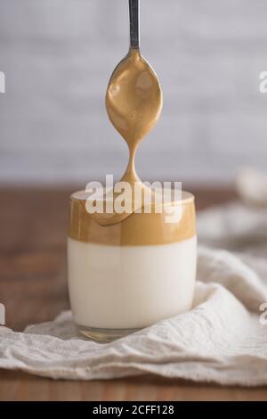 Von oben abgeschnitten gesichtslose Person Hand mit Teelöffel Zugabe Schlagsahne Kaffee in kalten hausgemachten Dalgona Getränk auf weiße Serviette gelegt In Holztisch Stockfoto