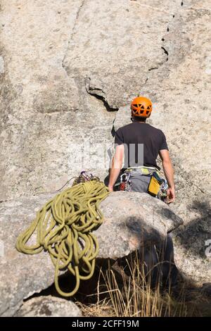 Ein junger kaukasischer Kletterer mit orangefarbenem Helm starrt Auf dem Gipfel des Berges, zu dem er geht Klettern Stockfoto