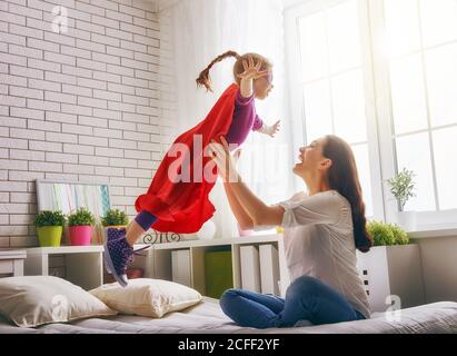 Mutter und ihr Mädchen spielen zusammen. Mädchen in einem Superman's Kostüm. Das Kind hat Spaß und springt auf dem Bett. Stockfoto