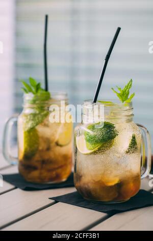 Zwei Mojitos-Cocktails, zubereitet mit Limette, Minze, Rum, Soda und Eis in Steinmetzgefäßen mit natürlichem Licht, im Freien Stockfoto