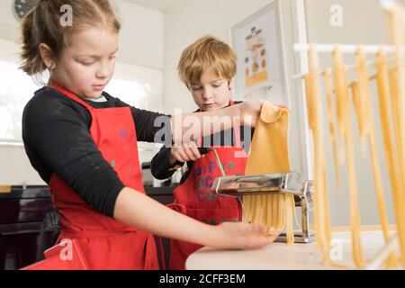 Ein kleines Mädchen mit älteren Bruder mit Pasta-Maschine, während Zubereitung von hausgemachten Nudeln in der heimischen Küche Stockfoto