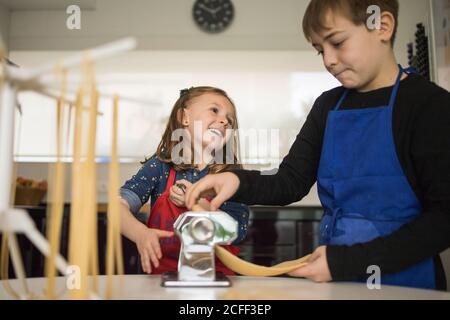 Ein kleines Mädchen mit älteren Bruder mit Pasta-Maschine, während Zubereitung von hausgemachten Nudeln in der heimischen Küche Stockfoto