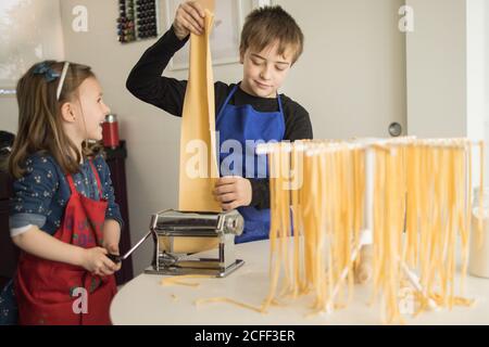 Ein kleines Mädchen mit älteren Bruder mit Pasta-Maschine, während Zubereitung von hausgemachten Nudeln in der heimischen Küche Stockfoto