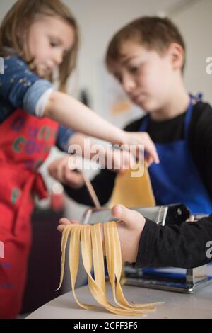 Ein kleines Mädchen mit älteren Bruder mit Pasta-Maschine, während Zubereitung von hausgemachten Nudeln in der heimischen Küche Stockfoto