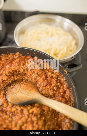 Von oben Nahaufnahme der Pfanne mit traditionellen Bolognese Sauce gelegt Auf dem Küchentisch neben dem Topf mit gekochter Pasta Stockfoto