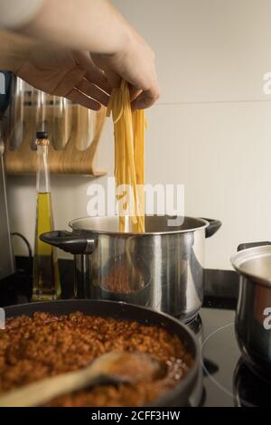 Crop Person setzen frische hausgemachte Nudeln in Metall-Topf mit Kochendes Wasser beim Zubereiten des Abendessens in der Küche Stockfoto