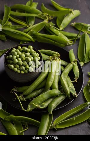 Geschälte, frische Erbsen und Erbsen auf dunklem Grund Stockfoto