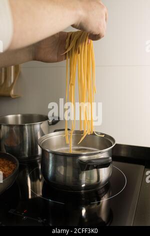 Crop Person setzen frische hausgemachte Nudeln in Metall-Topf mit Kochendes Wasser beim Zubereiten des Abendessens in der Küche Stockfoto