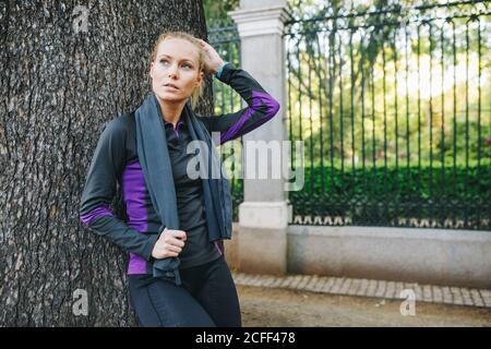 Junge blonde kaukasische Frau, die sich nach dem Joggen auf einem Baum lehnt Stockfoto