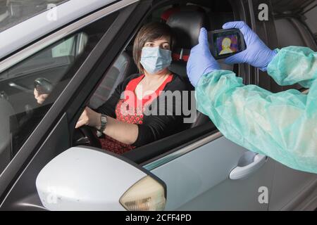 Crop Arzt in medizinischen Handschuhen Messung der Temperatur der weiblichen Fahrer Bei der Verwendung von Infrarotkamera während Coronavirus-Epidemie Stockfoto