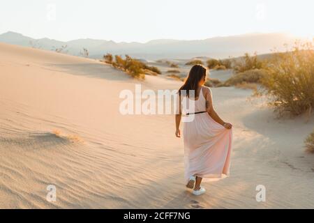 Rückansicht einer jungen Frau, die in der Wüste läuft und Spuren in trockenen Sanddünen im Death Valley hinterlässt Stockfoto