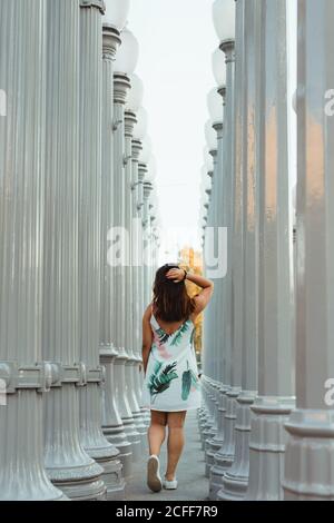 Rückansicht einer jungen aktiven Frau, die in Los Angeles in einer Reihe mit einer hohen silbernen Laterne läuft und Haare berührt Stockfoto