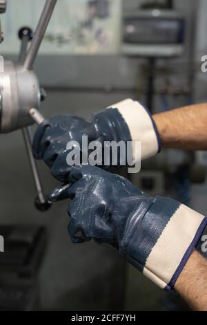 Crop unkenntlich männlichen Meister in Gummihandschuhe Drehen Industriemaschine Ventil bei Arbeiten im Werk Stockfoto