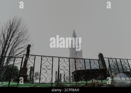 Von unten von nebligen Friedhof mit Zaun und alte Kirche Am bewölkten Tag Stockfoto