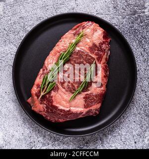 Frisches rohes Rindersteak auf schwarzem Teller, Draufsicht. Stockfoto