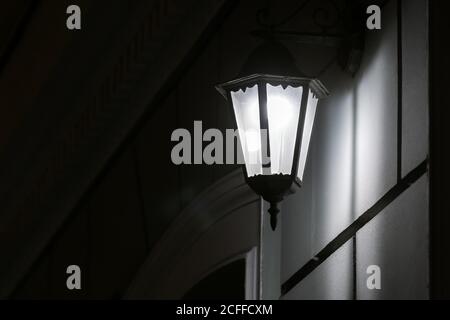 Schwarze Eisen-Retro-Laterne mit transparentem Glas an der Wand der Fassade des Gebäudes beleuchtet die Architektur der Stadt in der Nacht, Stockfoto