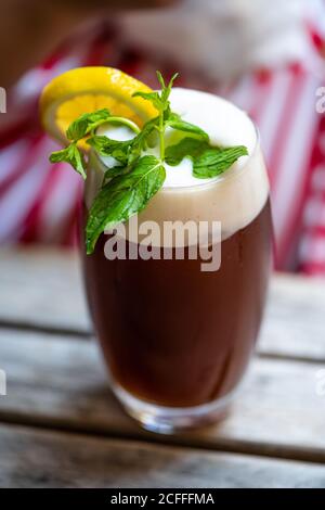 Schaumiger Eistee mit Minzblättern in serviert mit großem Glas / Ice Tea Foam auf Holztisch. Bereit zum Servieren und Trinken. Stockfoto