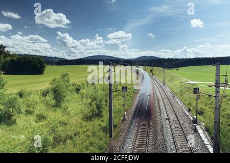 Drone Blick auf majestätische Landschaft der Zug Reiten entlang der Eisenbahn Umgeben von grünen Feldern und Bergen an sonnigen Tagen Stockfoto